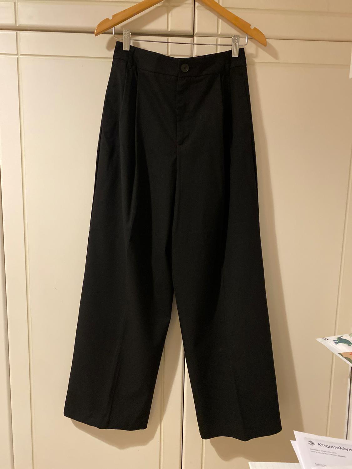 Black wide-leg trousers hanging on a wooden hanger against a backdrop of white doors.