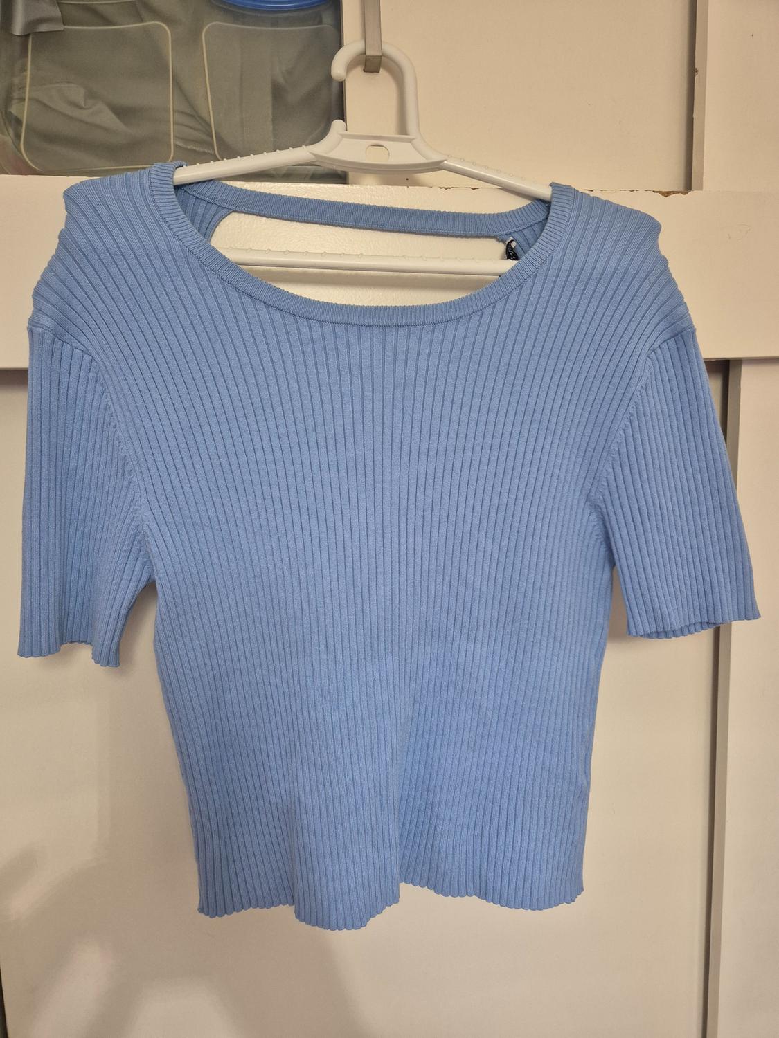 Blue short-sleeved, ribbed t-shirt hanging on a white hanger against a light background.