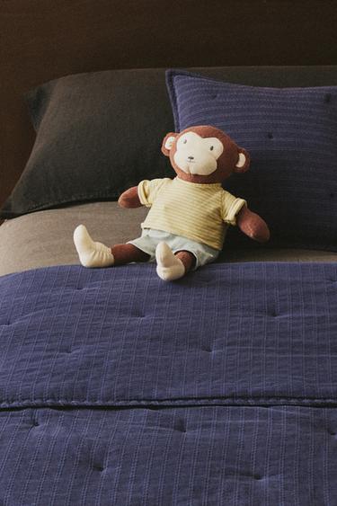 Navy blue children's duvet with a striped jacquard design, accompanied by a monkey soft toy wearing a yellow T-shirt.