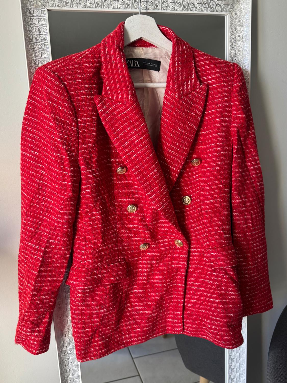 Red double-breasted jacket with gold buttons, hanging on a white hanger in front of a mirror with a decorative frame.