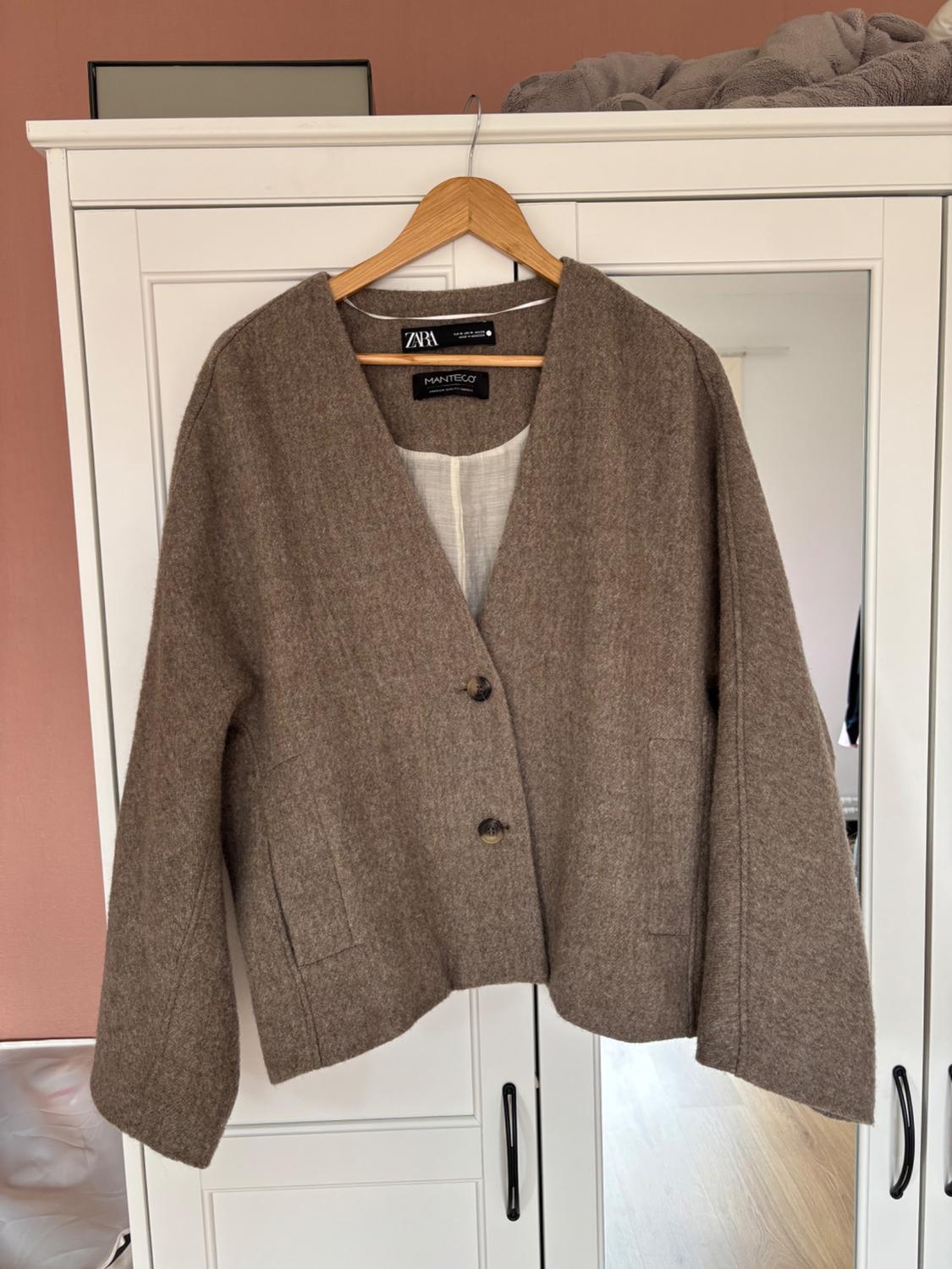 Brown V-neck button-up jacket, hanging in a white wardrobe. The ZARA and MANTECO labels can be seen on the inside.