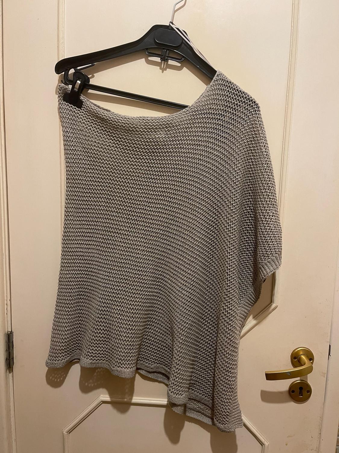 Light grey open-knit top hanging on a black hanger over a white door with a gold handle. Casual style.