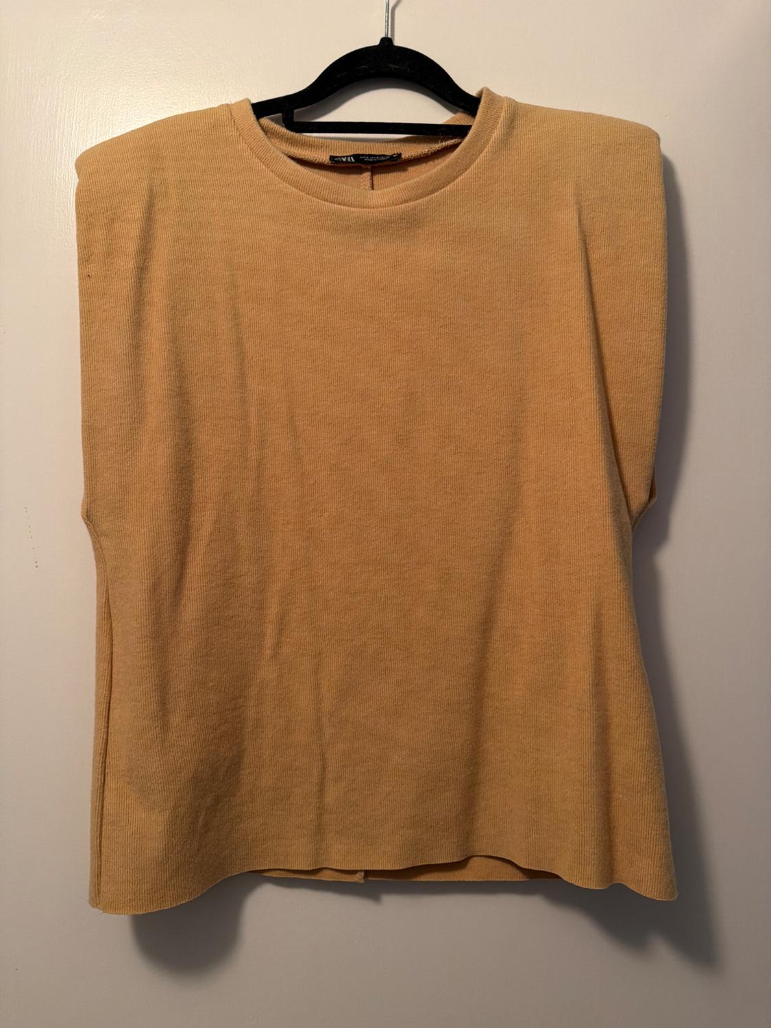 Beige short-sleeved jumper hanging on a black hanger against a white background.