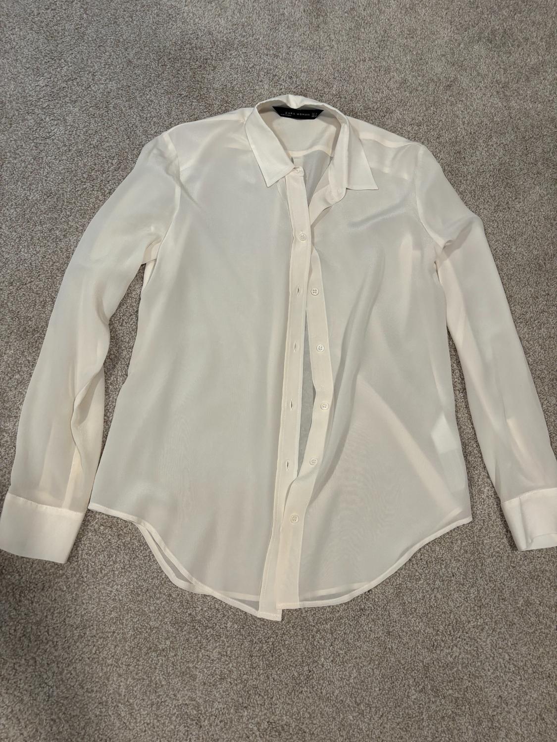 White long-sleeved button-down shirt, placed on a gray rug.
