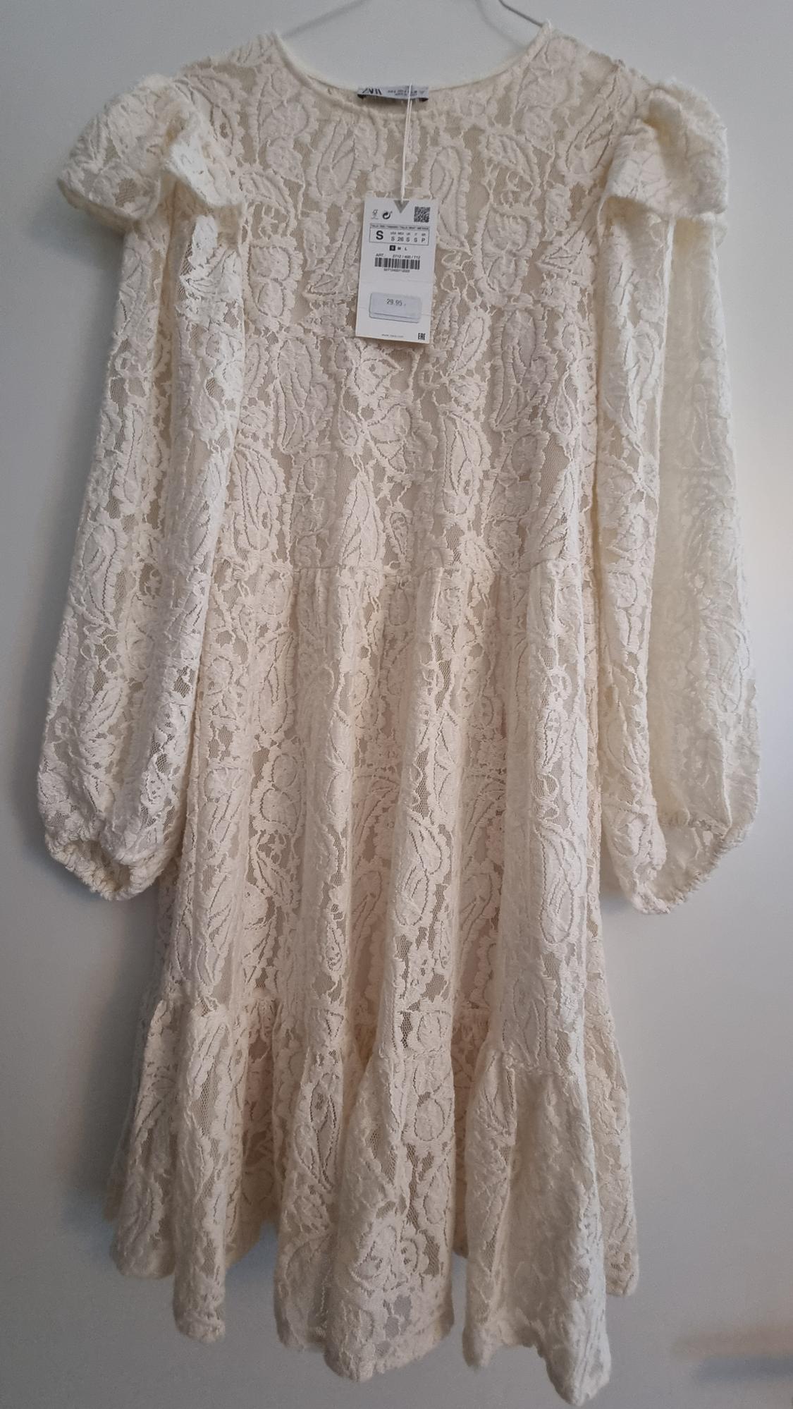 White lace dress with puffed long sleeves, hanging on a hanger. Visible tag with price of 29.95.