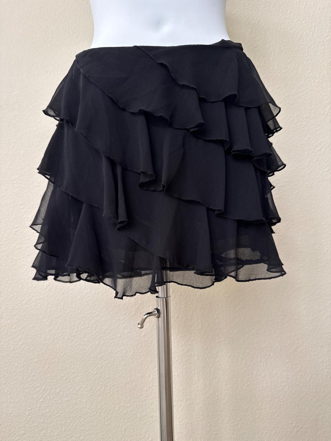 Black mini skirt with ruffled layers in semi-sheer fabric, displayed on a white mannequin with a metal stand against a light background.
