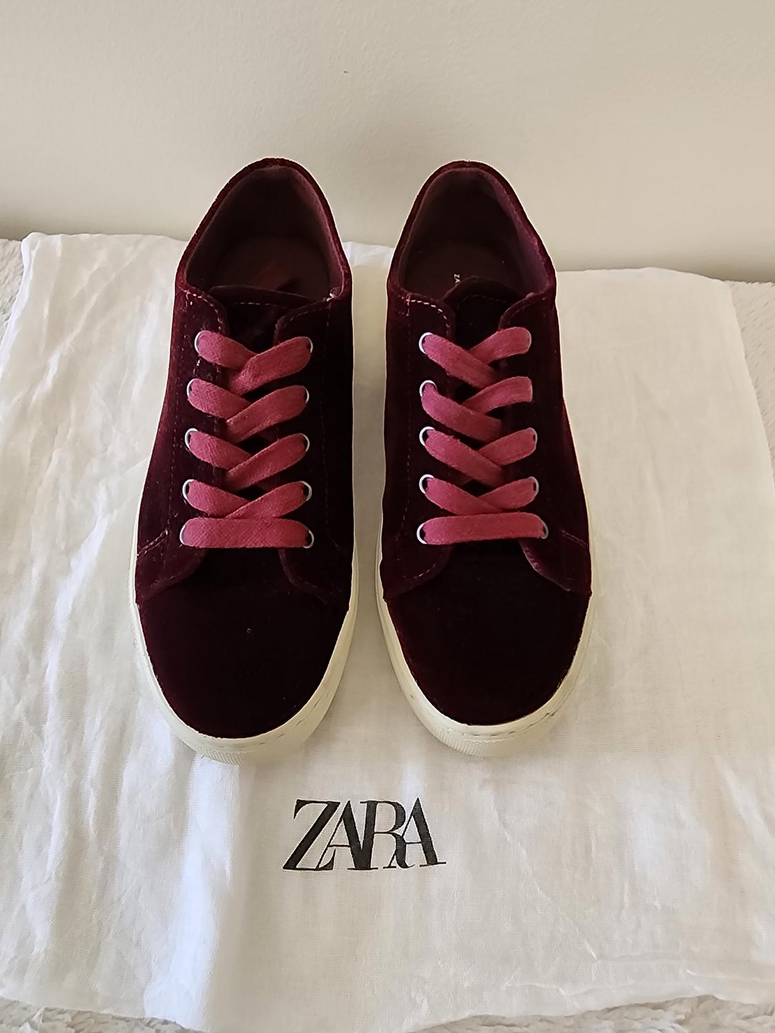 Front view of burgundy sneakers with pink laces on a case with the text 'ZARA'.