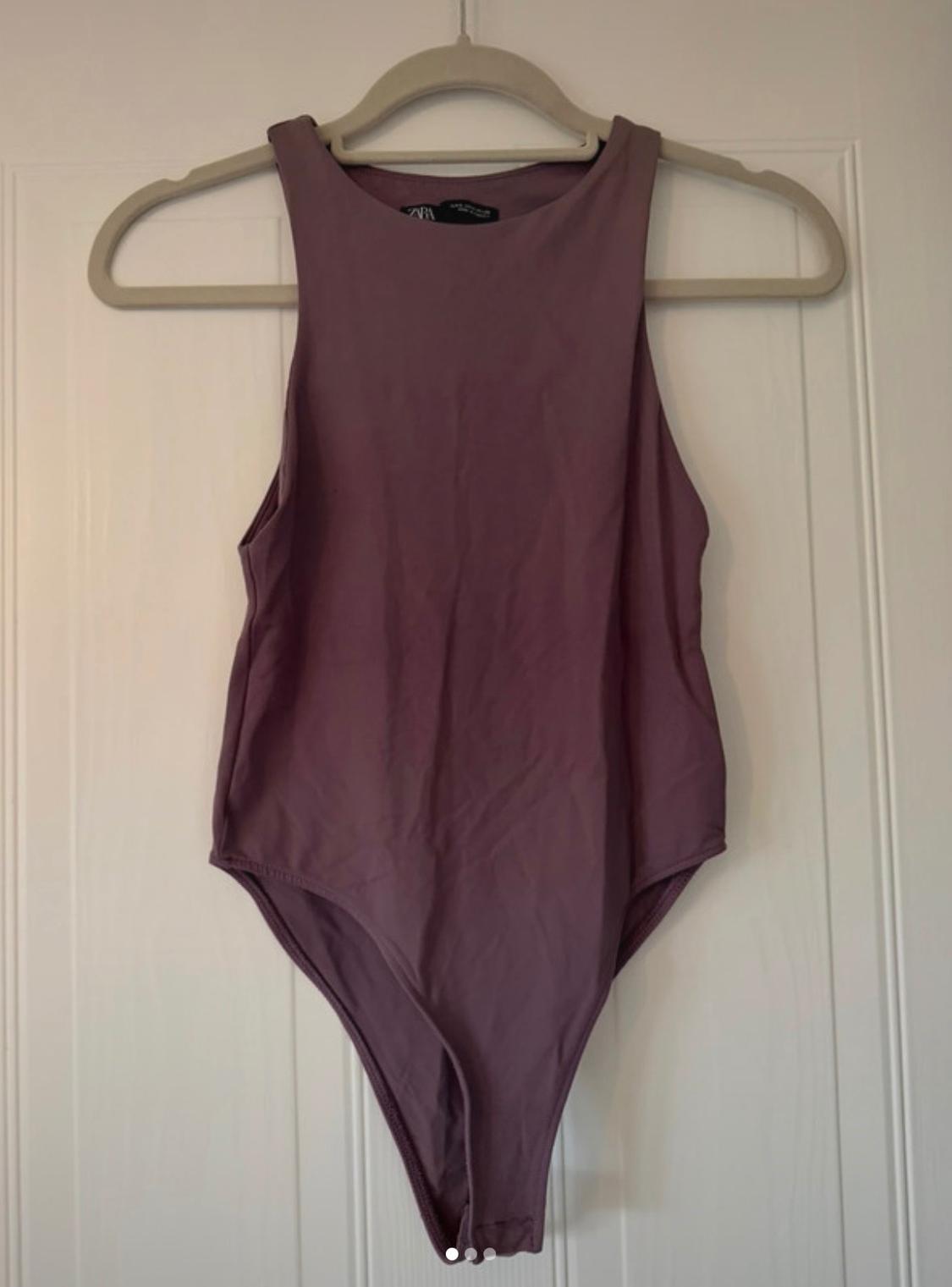 Mauve sleeveless bodysuit hanging on a hanger on a white door. Text ZARA on the label.