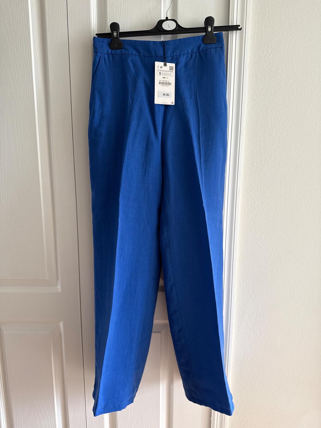 Blue pants hanging on a black hanger with a price tag of 49.90. White door background.