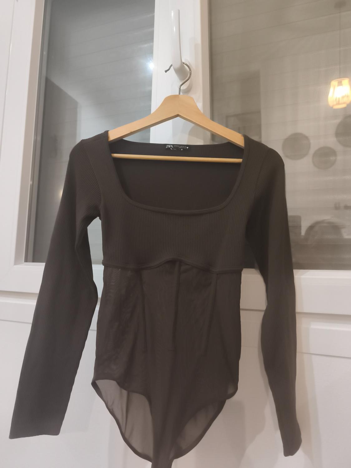 Black long-sleeved bodysuit hanging on a wooden hanger in front of a white window.