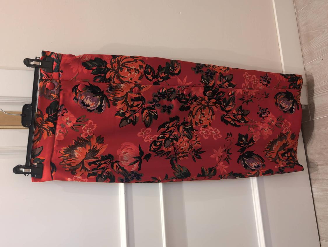Red skirt with dark floral print and front buttons, hanging on a black hanger over a white door.