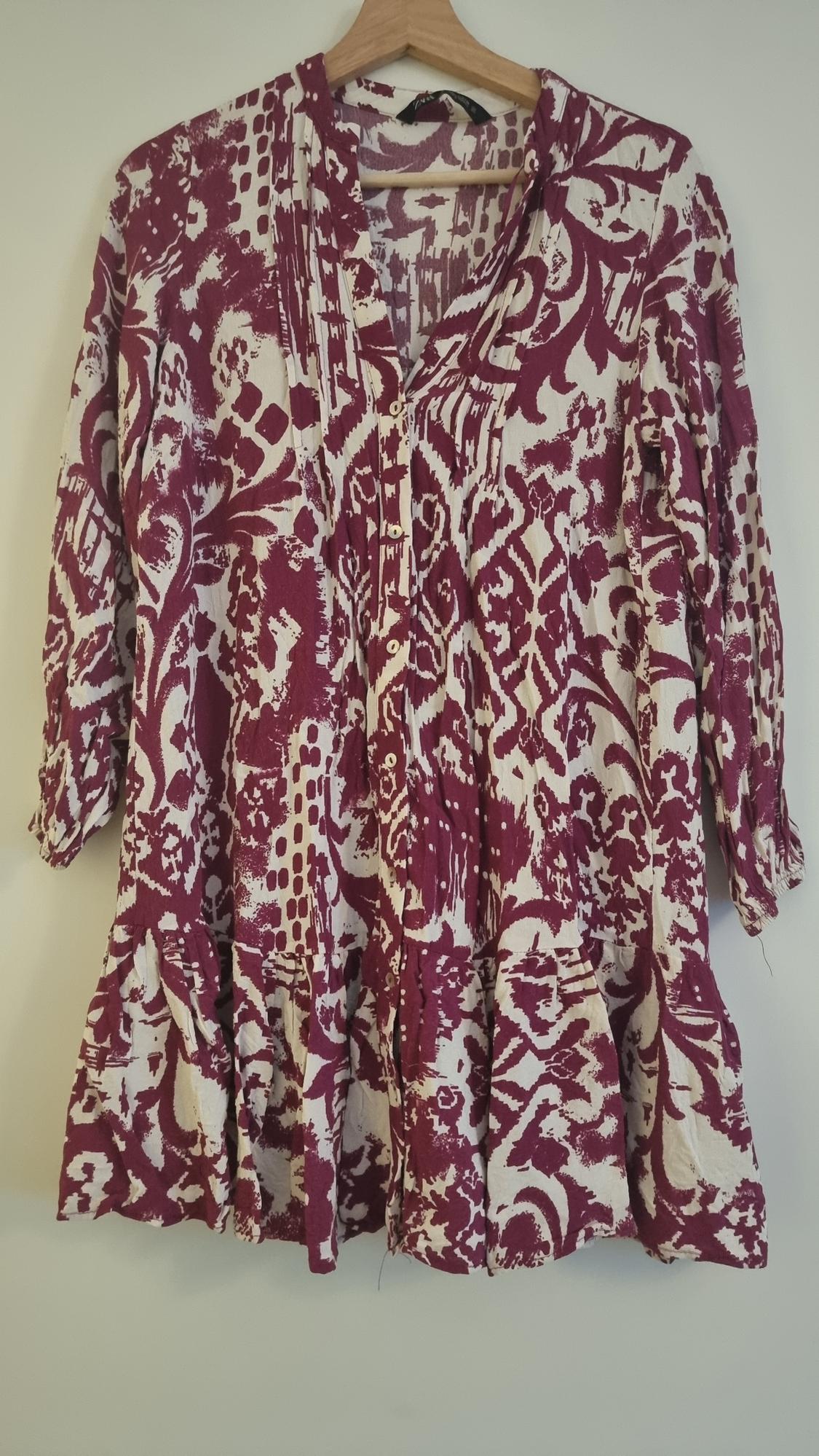Long-sleeved blouse with a floral print in burgundy and white tones, hanging on a wooden hanger against a white background.