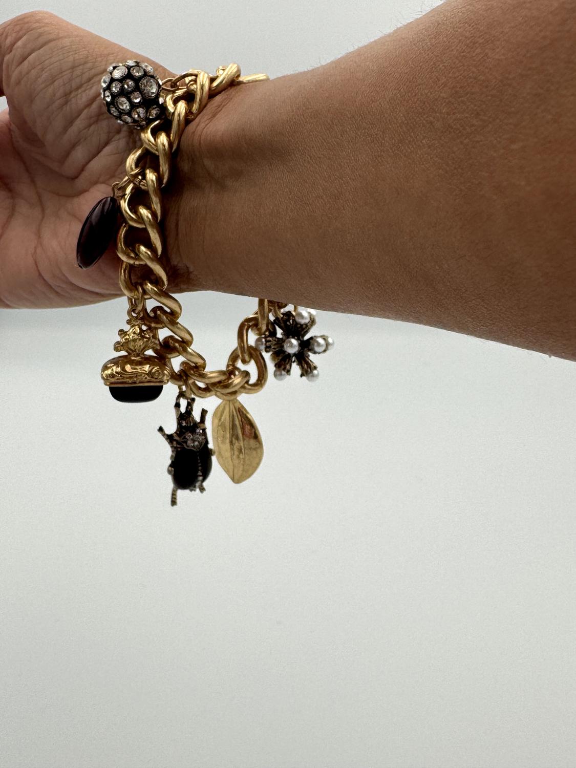 Golden bracelet with insect and leaf charms on a wrist. White background and ring with sparkling stones on the finger.