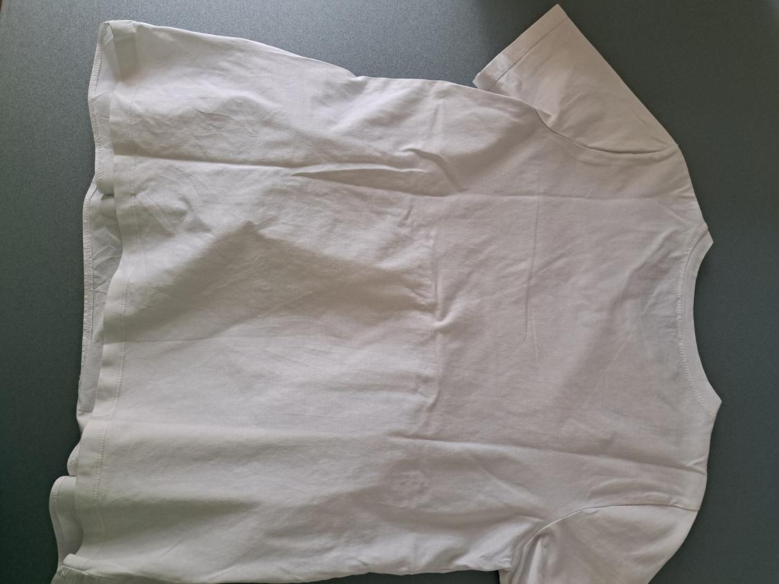 White short-sleeved t-shirt laid out on a grey surface, showing the back and the garment's simple design.