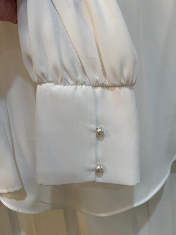 White blouse cuff with pearl buttons, soft and pleated fabric. White background, focus on the sleeve design detail.
