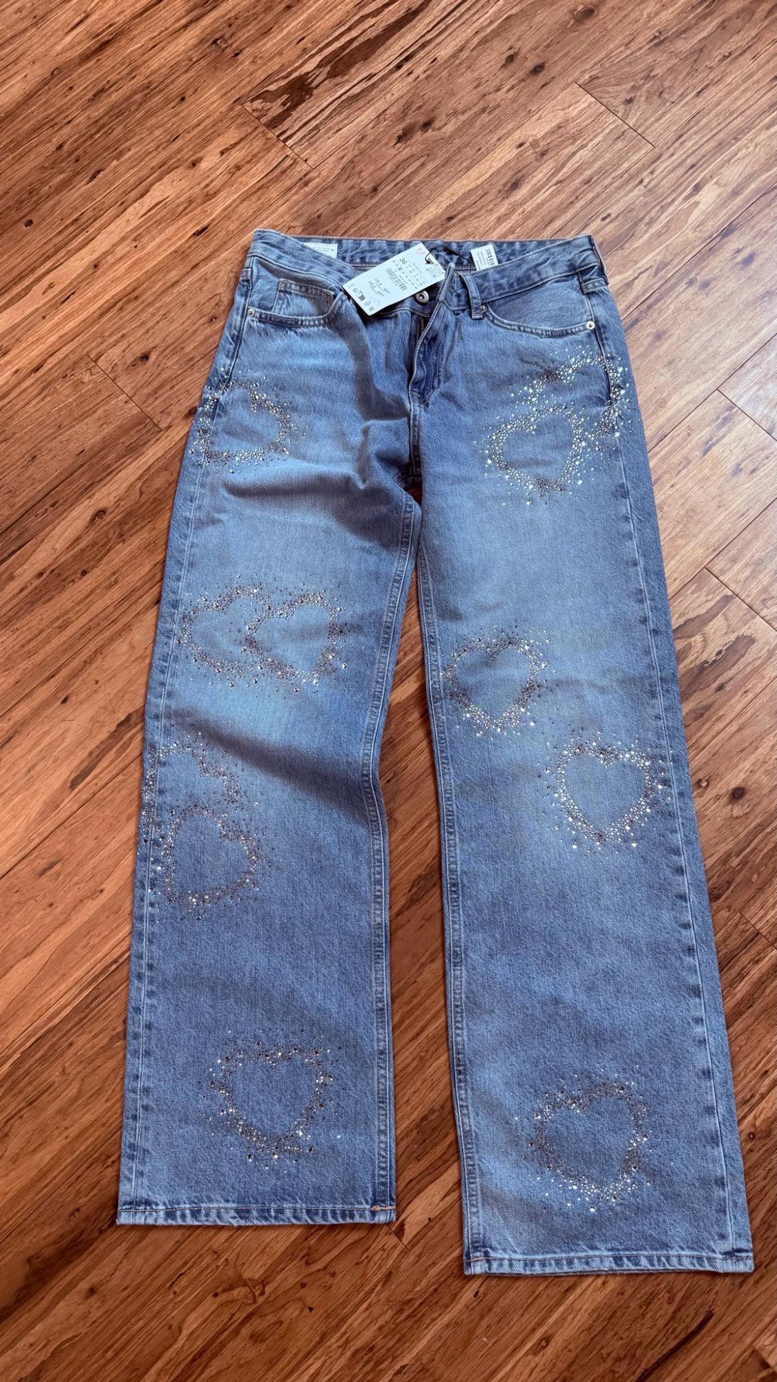 Light blue jeans decorated with sparkly rhinestone hearts, laid out on a wooden floor.