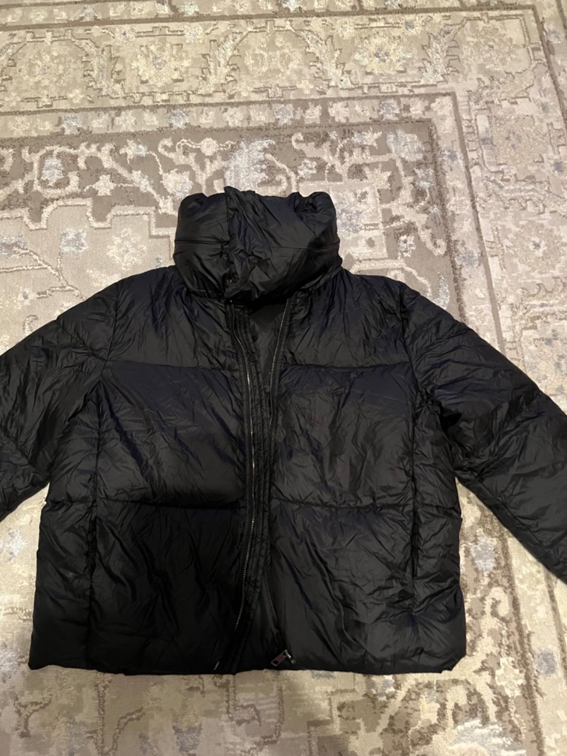 Black quilted jacket with a hood on a geometric design rug in beige and gray tones.