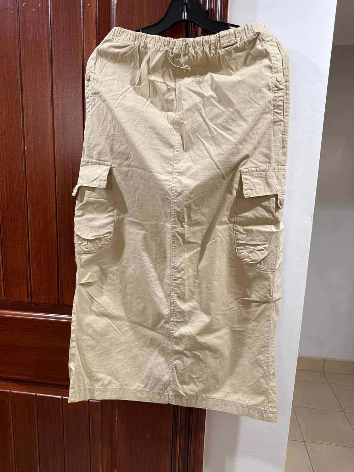 Beige cotton skirt with cargo pockets, hanging on a black hanger in front of a brown wooden door.
