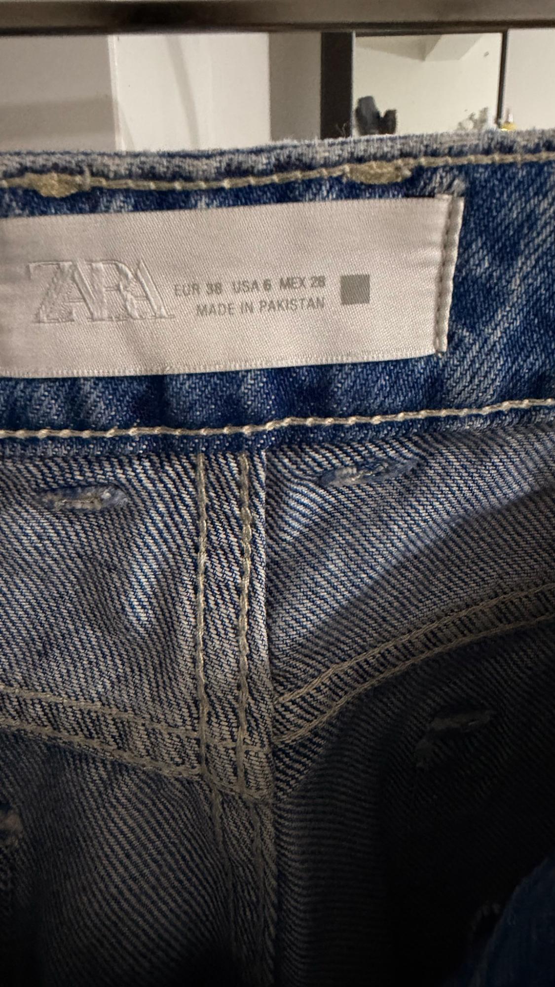 Close-up of the inside of a blue pair of jeans with stitching and a white label: ZARA EUR 38 USA 6 MEX 28 MADE IN PAKISTAN.