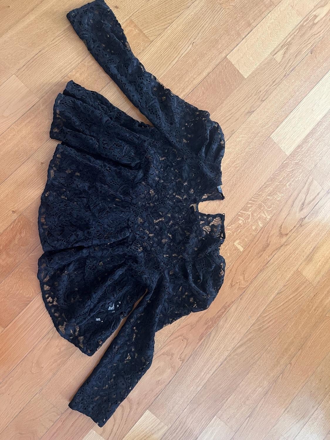 Black lace long-sleeved blouse laid out on a wooden floor.
