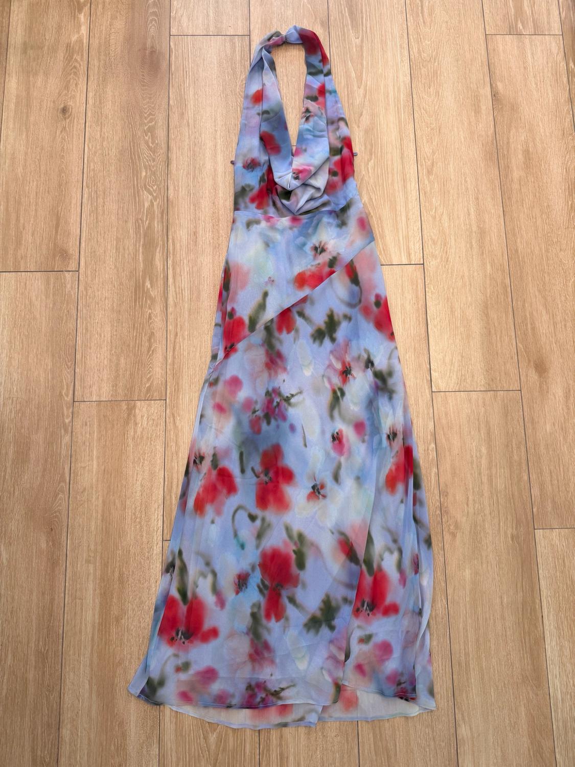 Draped halter-neck maxi dress with a red floral print on a blue background, laid out on a wooden floor.