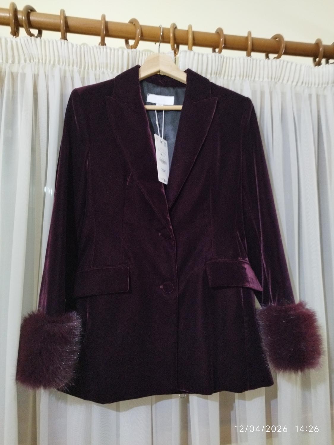 Purple velvet jacket with fur cuffs, hanging on a hanger in front of white curtains. Date on image: 12/04/2026 14:26.