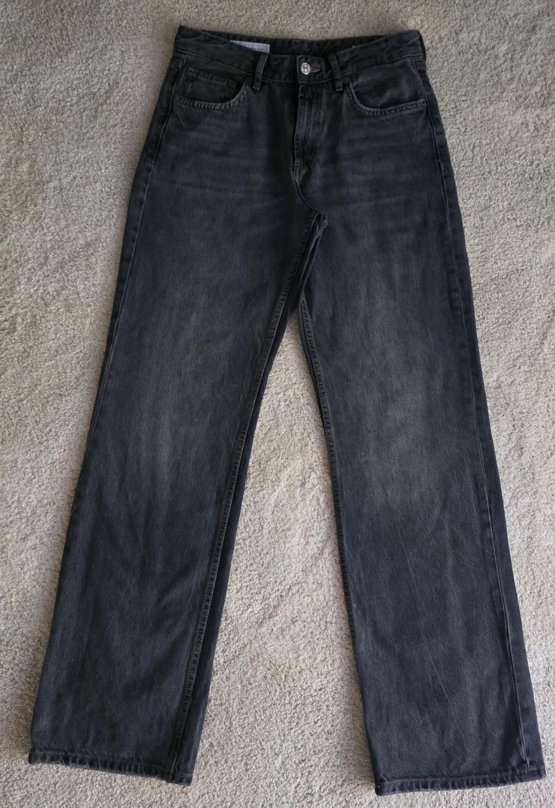 Worn black straight-leg jeans, laid out on a light-colored rug. Casual style and relaxed fit.