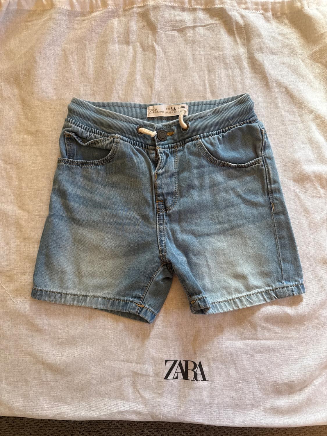 Light blue denim shorts with an elasticated waist and drawstring, on a white fabric bag with the Zara logo.