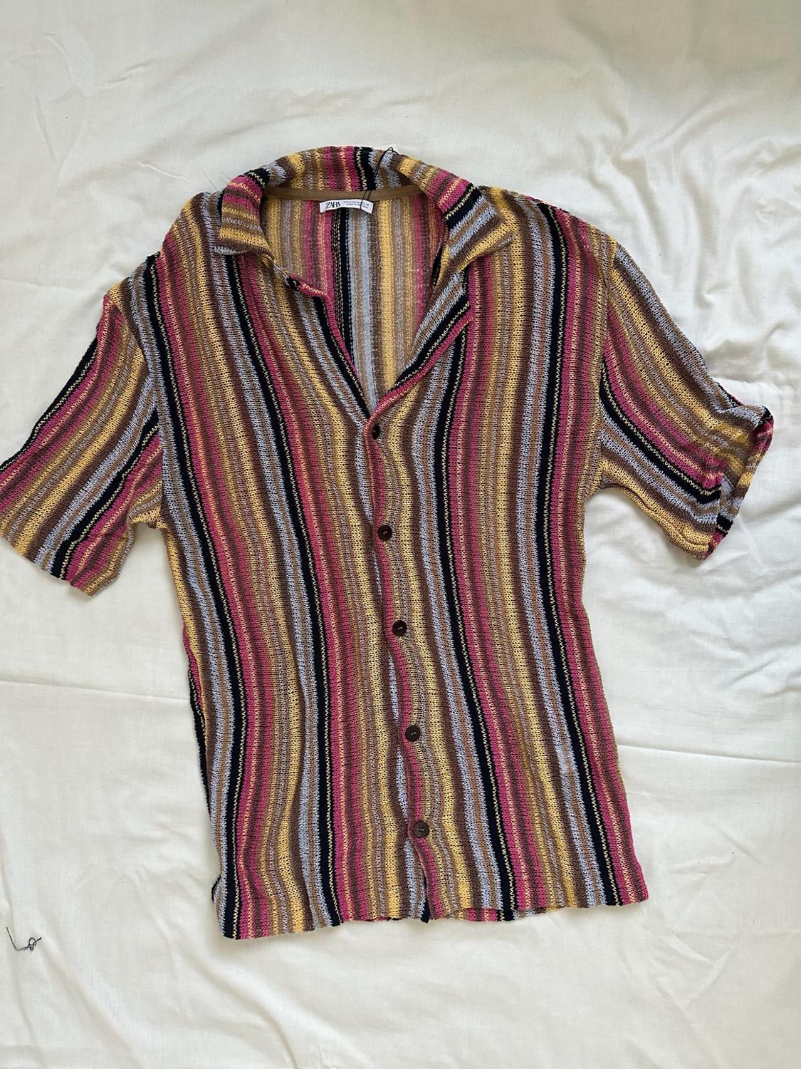 Short-sleeved knitted button-up shirt with multicoloured stripes on white crinkled fabric. ZARA label on the collar.