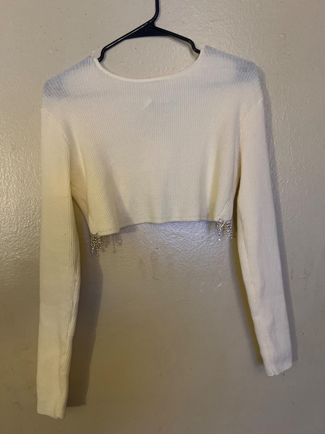 Front view of a short white sweater with long sleeves and a hanging detail on the hem.