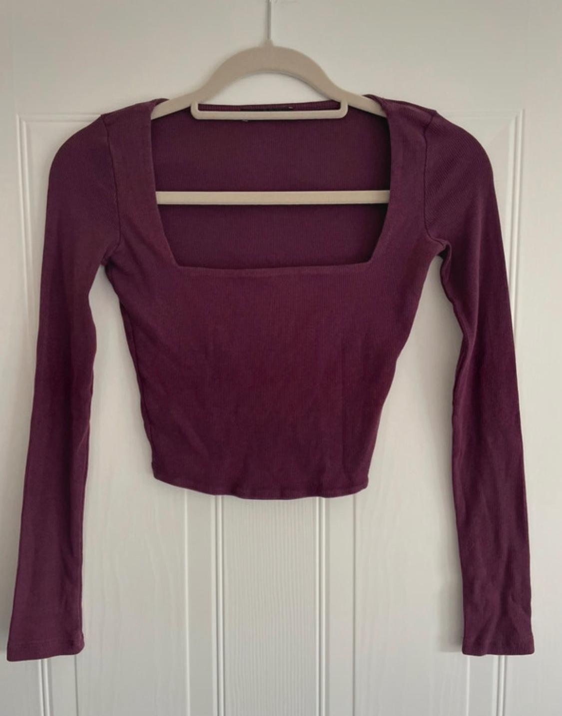 Dark purple ribbed knit long-sleeved top with a square neckline, hanging on a hanger over a white door.