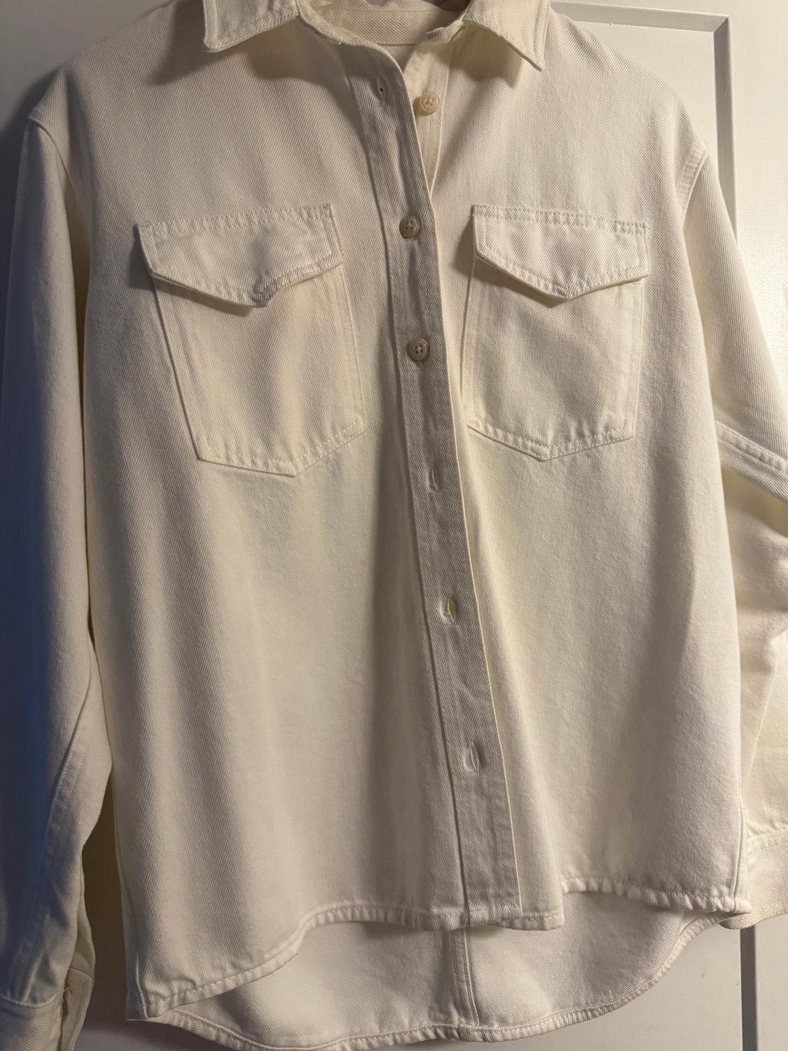 White, long-sleeved shirt with two front pockets and buttons, hanging on a white door.