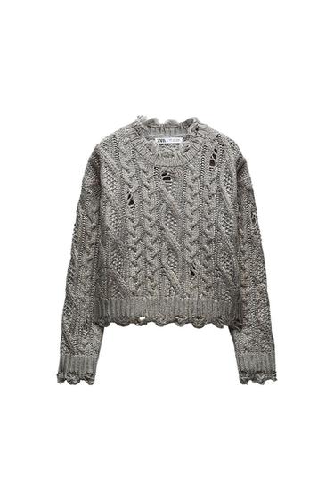 Gray, chunky knit sweater with cable knit design and scalloped edges. Visible tag on the neck with the brand name.