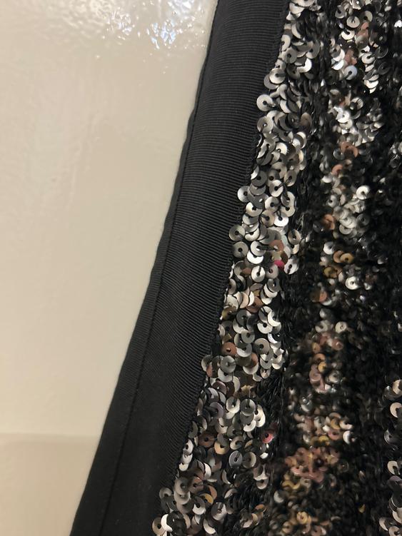 Detail of black fabric with shiny silver sequins in a vertical pattern. Light background and visible texture.
