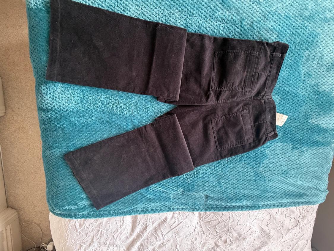Dark trousers folded to show the back pockets, on a turquoise blue blanket and white sheets in a relaxed home setting.