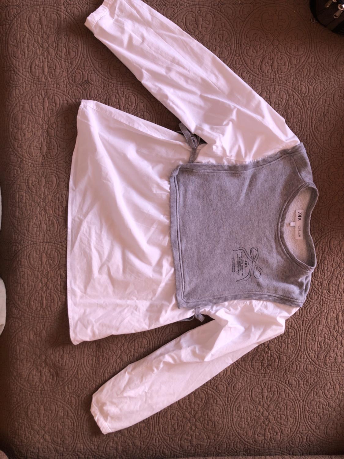 White shirt with layered grey top, bow graphic, ART. text and ZARA label. Flat lay photograph on textured brown fabric.
