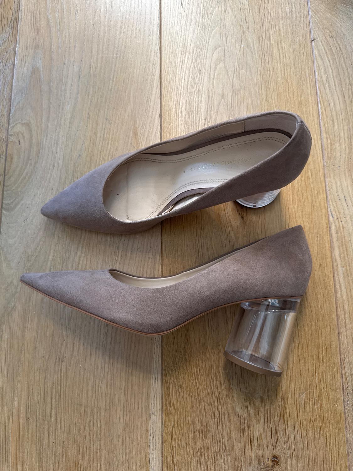 Brown low-heeled shoes with a pointed toe and clear heel on a light wooden floor.