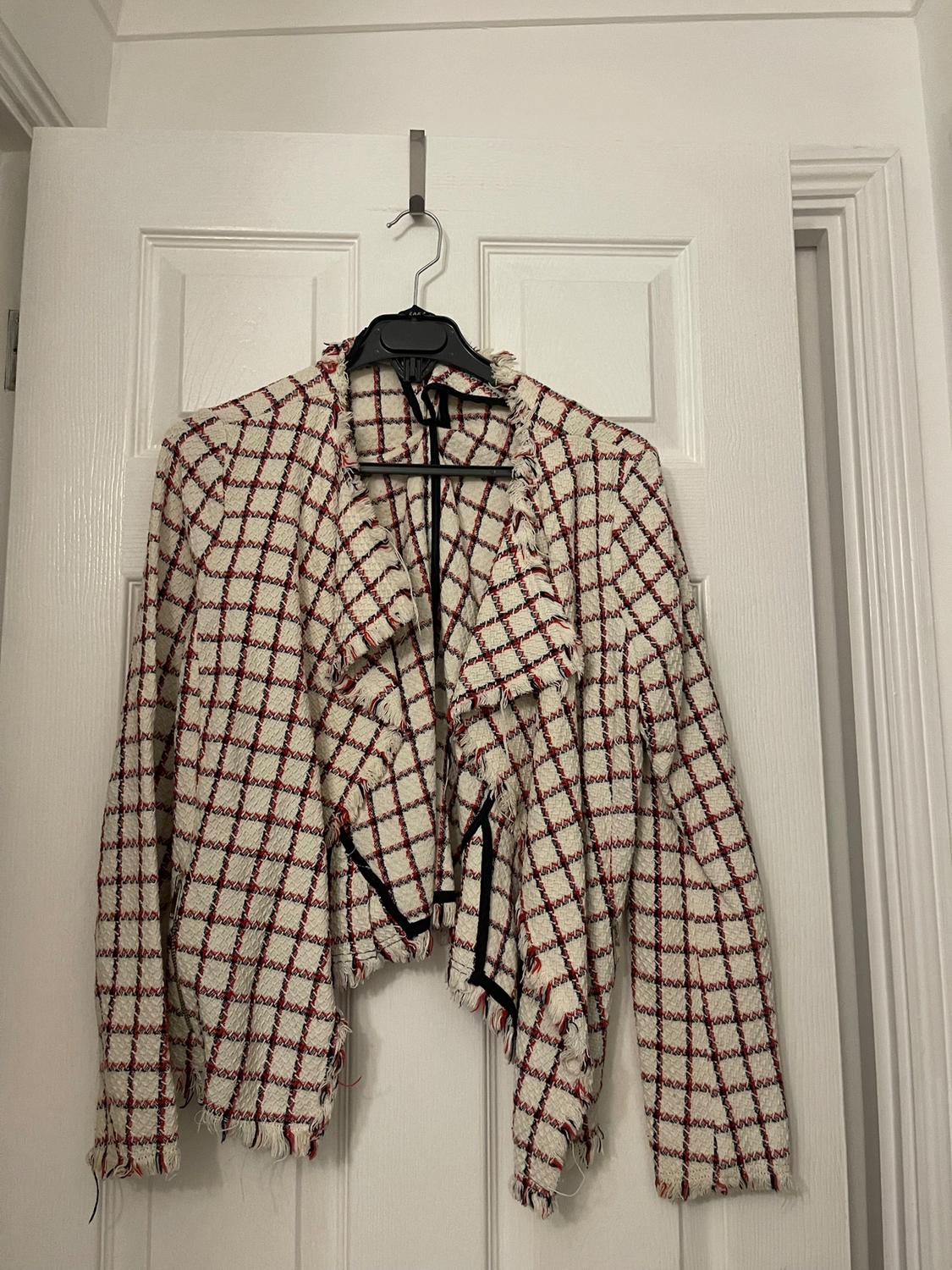 Red and white checked jacket with frayed edges, hanging on a white door with a black hanger.