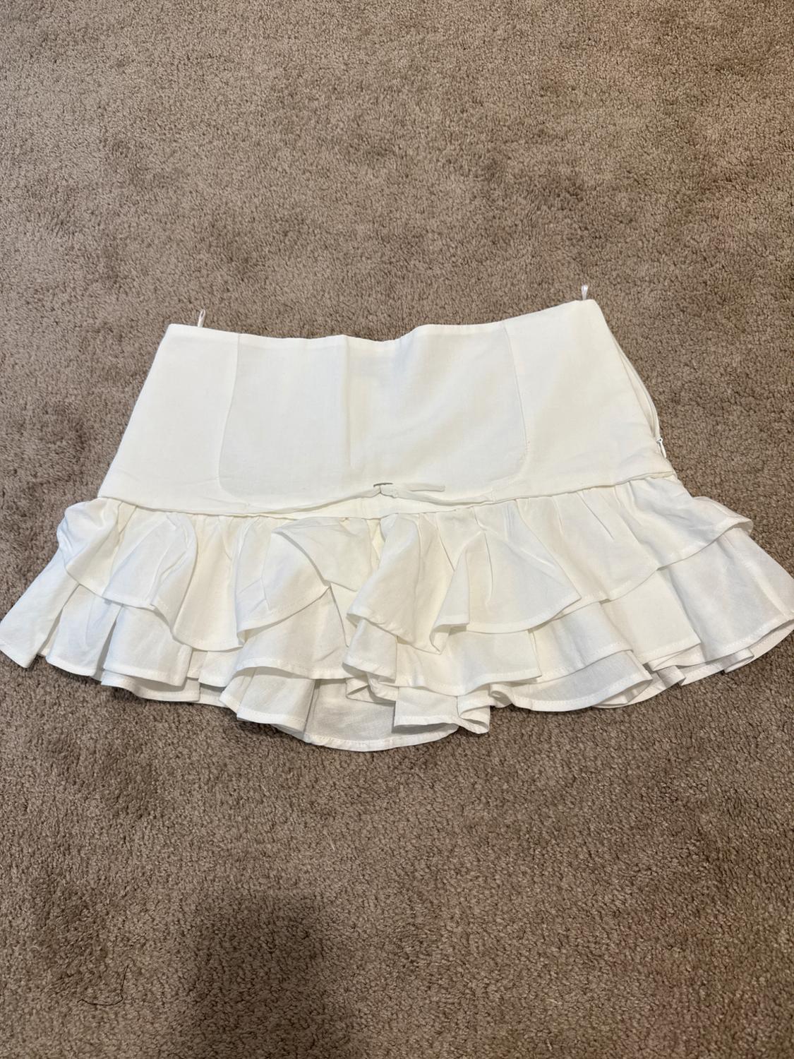 White miniskirt with ruffles at the bottom, placed on a brown rug.