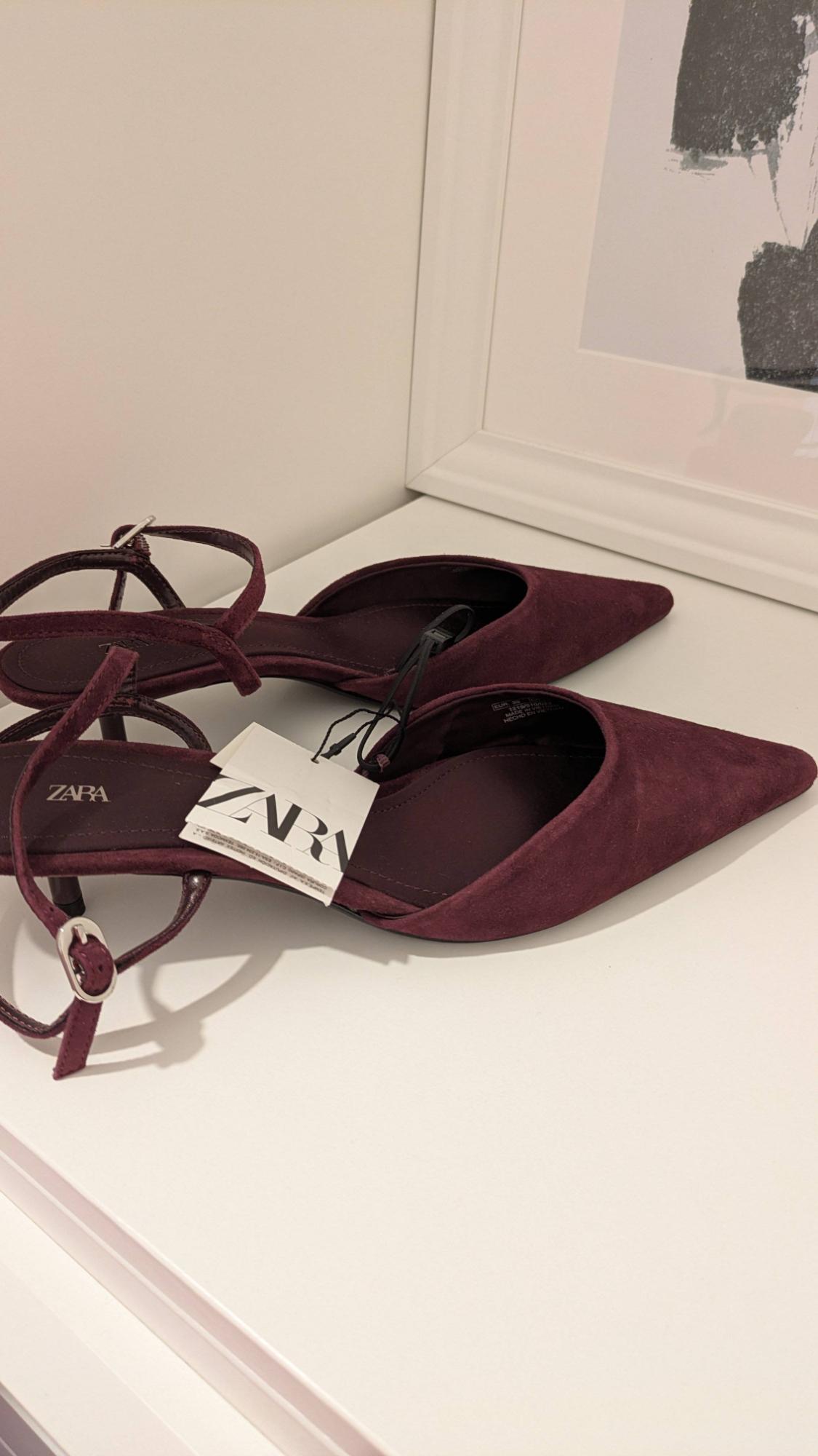 Burgundy low-heeled shoes with a pointed toe and adjustable strap. Visible label with the text "ZARA". Minimalist white background.