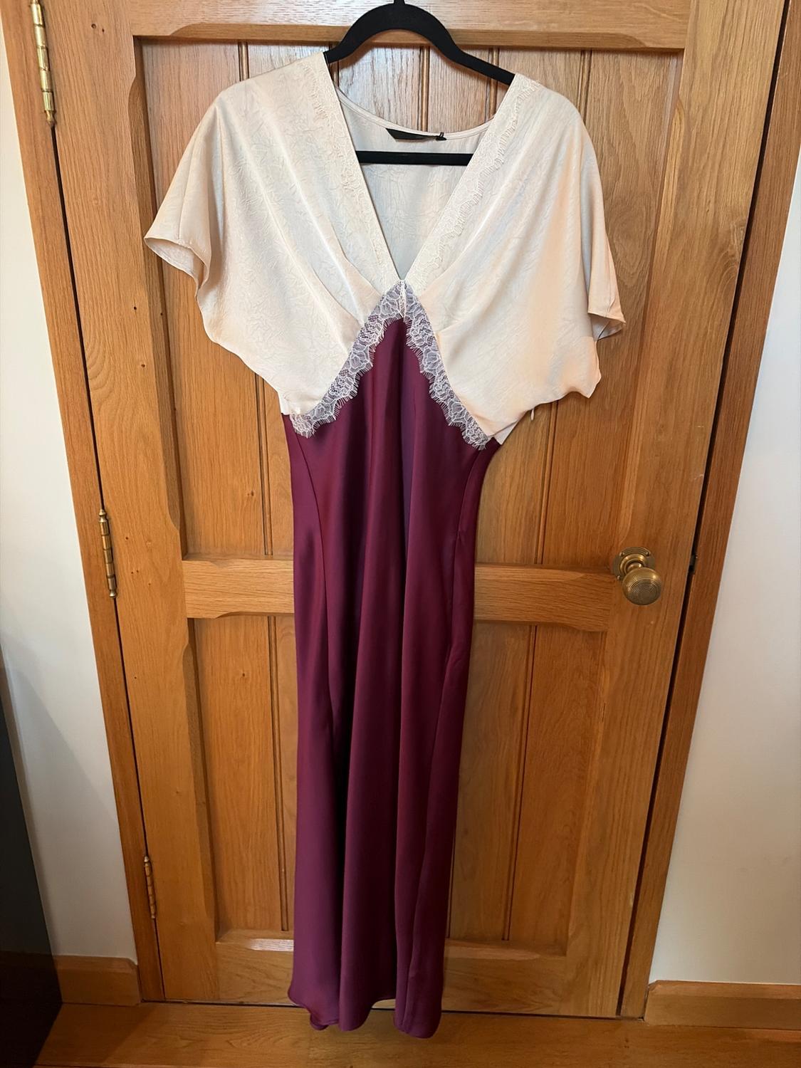 Dress hanging on a wooden door, with a white lace top and a long burgundy skirt.