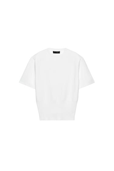 Front view of a white knitted round-neck top with short sleeves and shoulder pads. Ribbed hem.