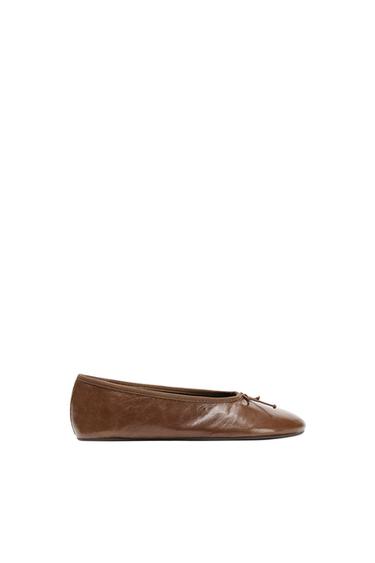 Brown leather flat ballet pumps with a small bow on the front, on a white background.