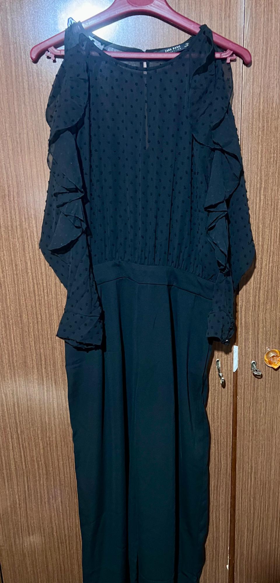 Black dress with long sleeves and frills, hanging on a red hanger in front of a wooden door.