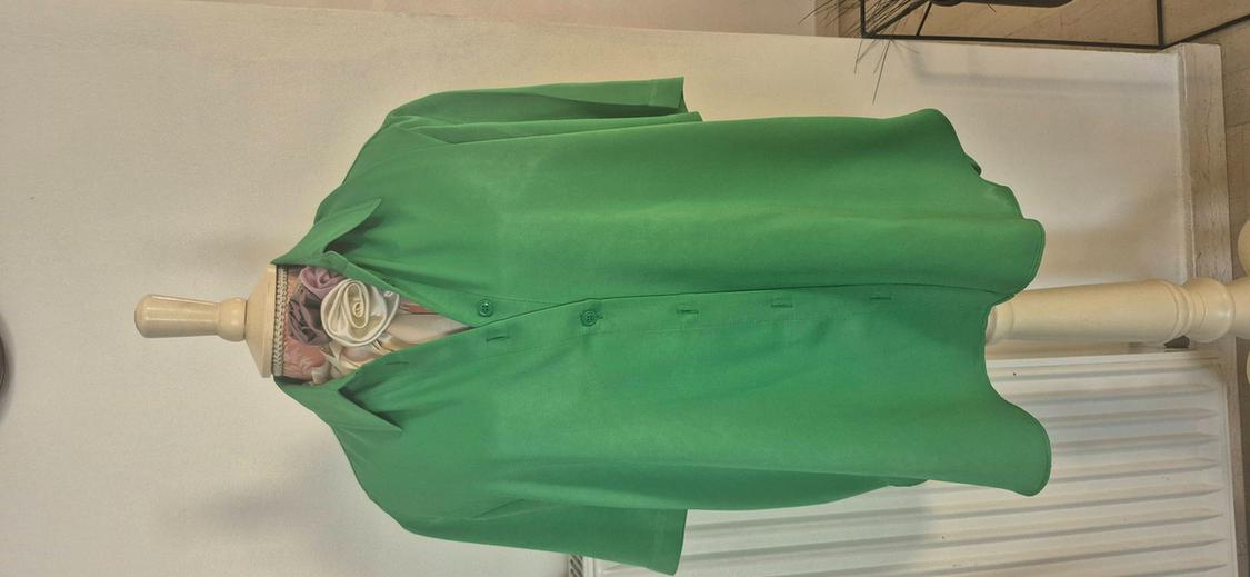 Green short-sleeved button-up shirt on a mannequin with a floral scarf at the neck, in front of a white wall.