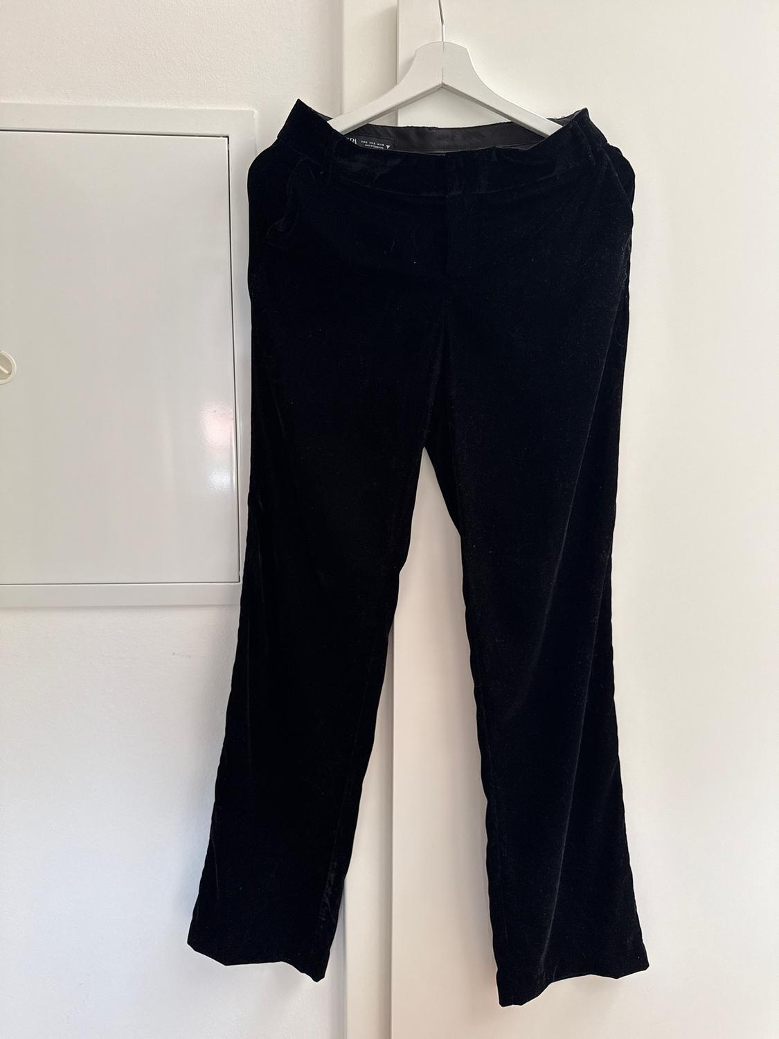 Black velvet trousers hanging on a white hanger over a white door. Minimalist and clean background.