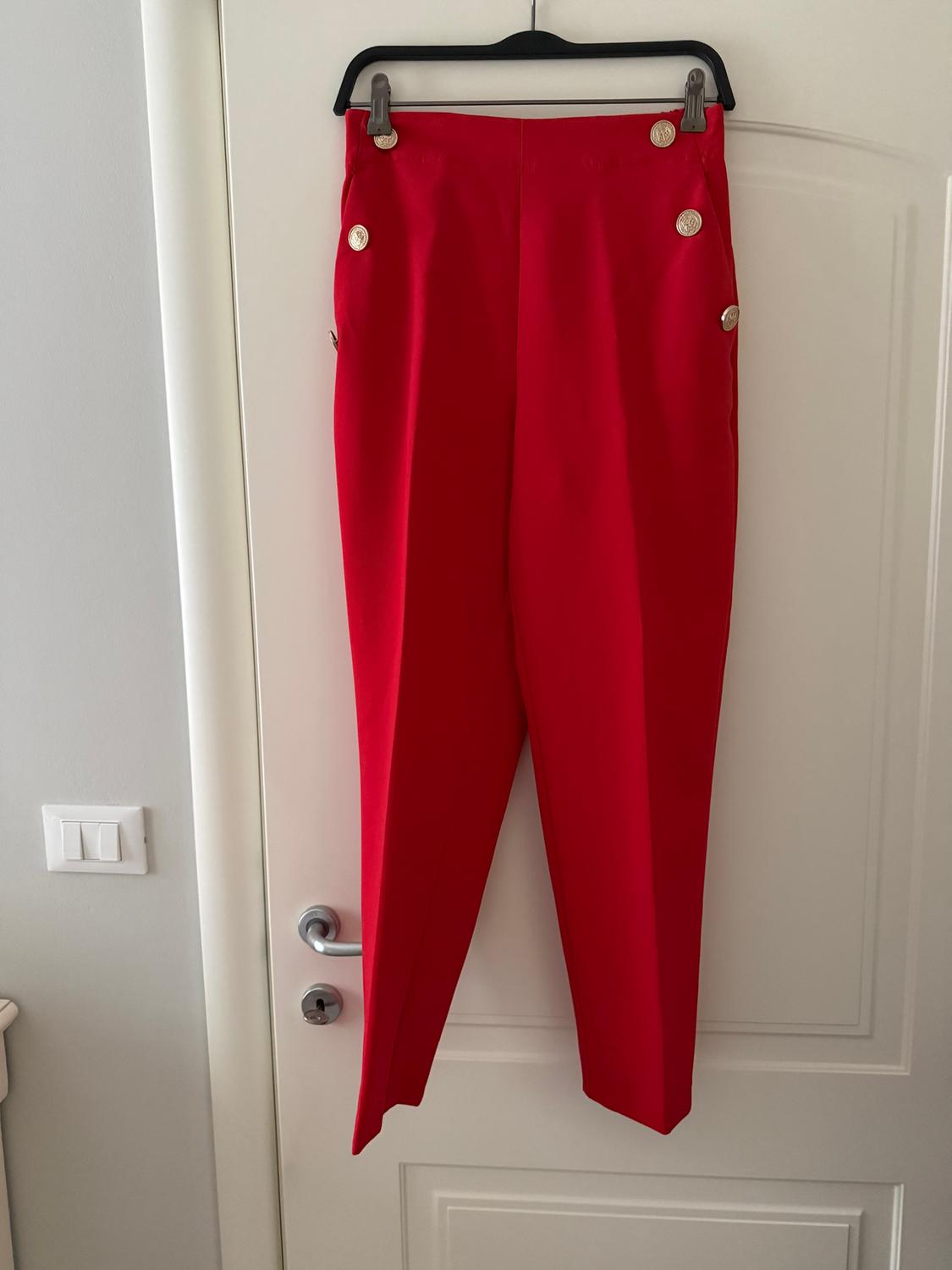 Red trousers hanging on a black hanger over a white door, with gold buttons on the waist and sides.