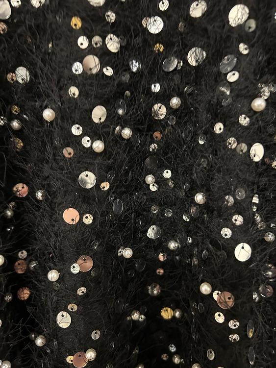 Black fabric with a fluffy texture adorned with shimmering silver and gold sequins, creating a dazzling effect.