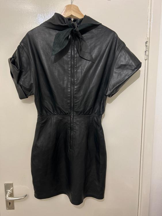 Black short-sleeved dress hanging on a wooden hanger. It has a bow at the neck and a back zip. White background.