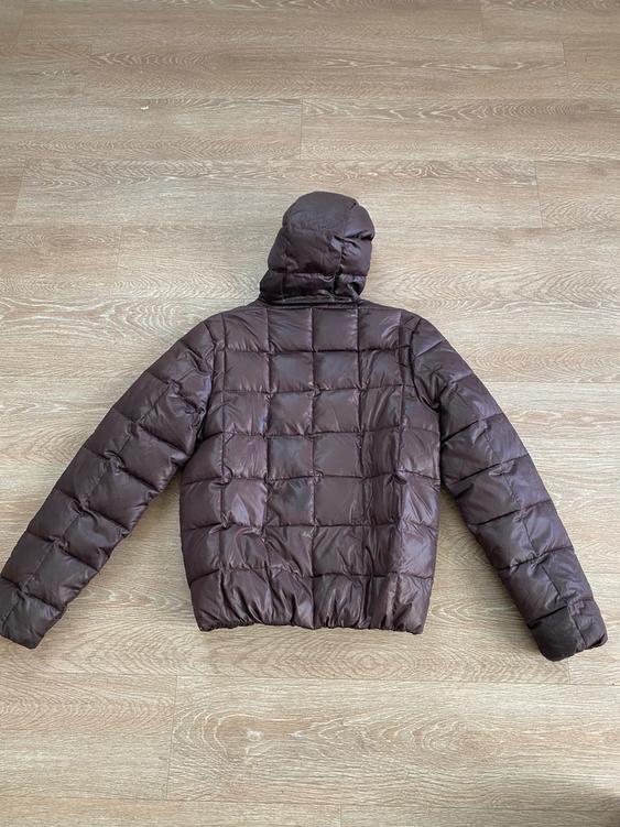 Brown padded jacket with a hood, seen from behind, on a light wooden floor.